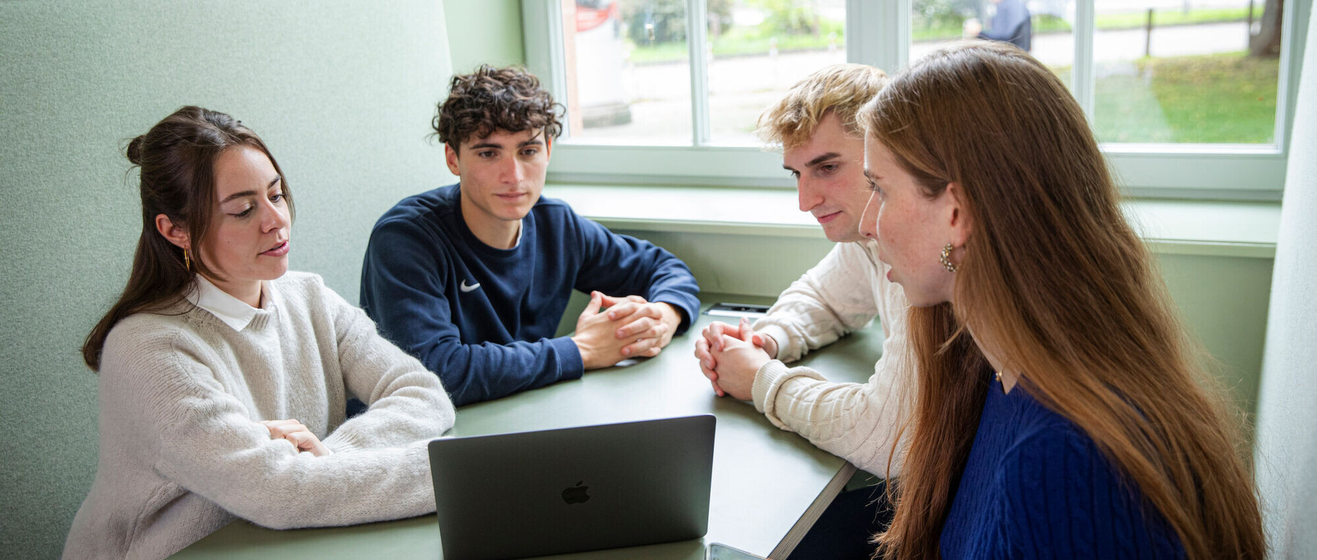 Four students are sitting together in front of a laptop