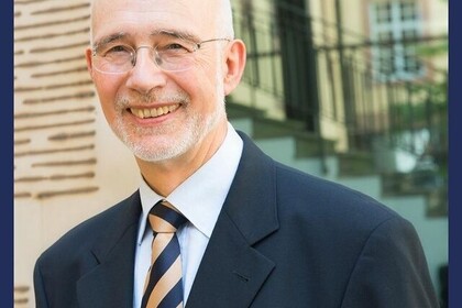 Thomas Puhl hat kurze graue Haare. Er trägt eine randlose Brille und einen dunklen Anzug. Unten steht: "Rektor des Jahres".