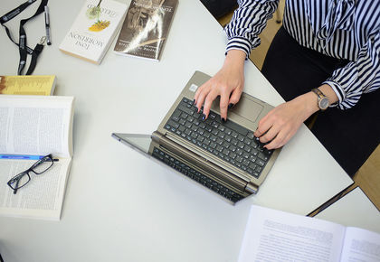 Eine Frau tippt in ihren Laptop und daneben liegen fünf Bücher.