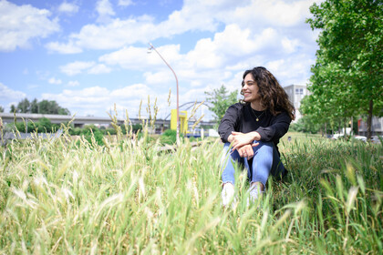 Eine Person sitzt auf einer Wiese und es ist gutes Wetter mit Sonnenschein und leichten Wolken.