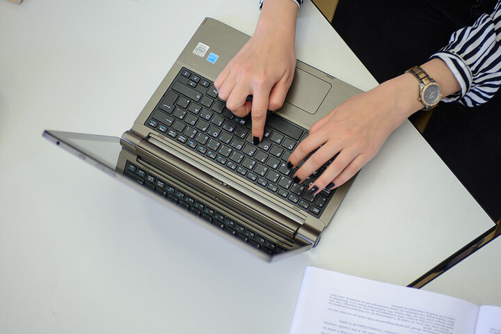 Zwei Hände tippen auf einem Laptop.