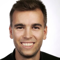 Tim Ostheimer hat kurze braune Haare. Er trägt ein dunkles Oberteil und lächelt in die Kamera.