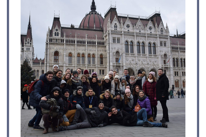 Eine große Menschengruppe posiert für ein Foto in einer Stadt. Oben rechts steht "Initiativen Universität Mannheim". 