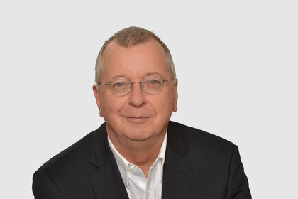 Prof. Weber hat kurze graue Haare und eine Brille. Er trägt ein Jacket und ein weißes Hemd.