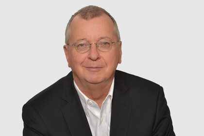 Prof. Weber hat kurze graue Haare und eine Brille. Er trägt ein Jacket und ein weißes Hemd.