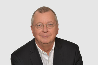 Prof. Weber hat kurze graue Haare und eine Brille. Er trägt ein Jacket und ein weißes Hemd.