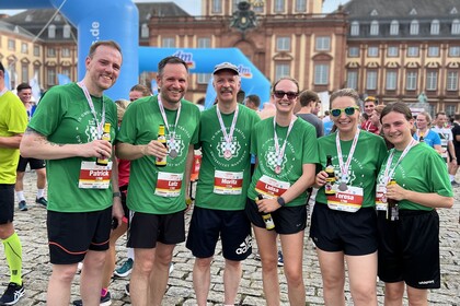 Sechs Läuferinnen und Läufer der Universität Mannheim in grünen T-Shirts mit Medaillen und Getränken vor dem Schloss.