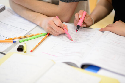 Zwei Studierende halten pinke Stifte in der Hand und zeigen sich etwas in einem Lernheft.
