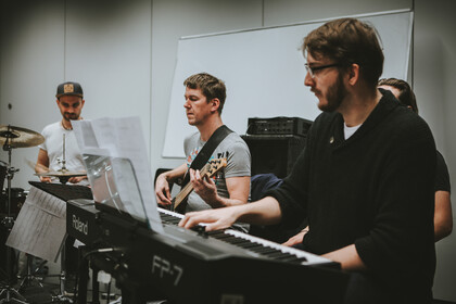Eine Person spielt Drums, eine Gitarre und eine andere Keyboard.