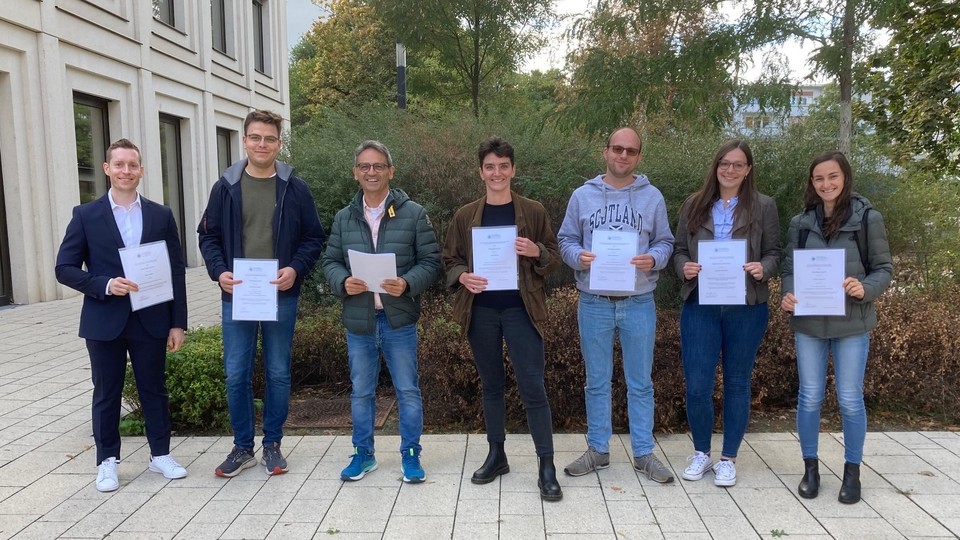 award winners Seven people are standing in the courtyard of B6, 30-32 and are holding papers.