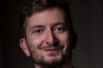 Portrait von Philipp Müller. Er trägt ein weißes Hemd und lächelt.