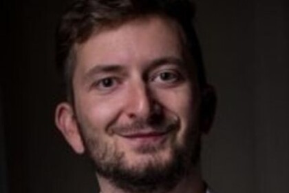 Portrait von Philipp Müller. Er trägt ein weißes Hemd und lächelt.