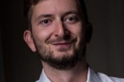 Portrait von Philipp Müller. Er trägt ein weißes Hemd und lächelt.