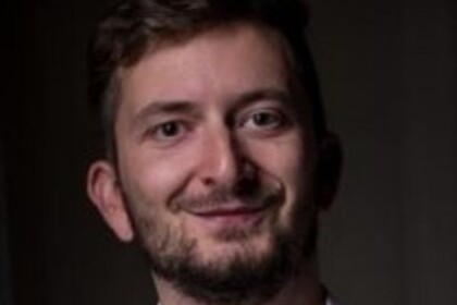 Portrait von Philipp Müller. Er trägt ein weißes Hemd und lächelt.