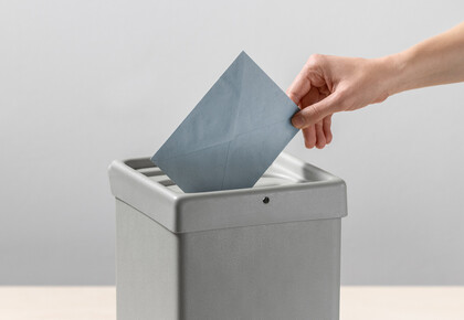 Eine Person steckt einen blauen Umschlag in eine Wahlurne.