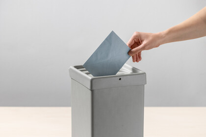Eine Person steckt einen blauen Umschlag in eine Wahlurne.
