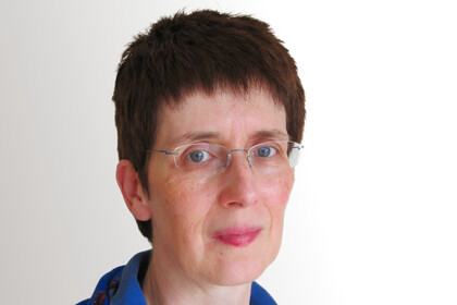 Angela Borgstedt trägt ein blaues Oberteil und eine Brille und lächelt leicht in die Kamera.