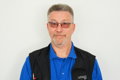Roland Hufnagel blickt ernst in die Kamera. Er trägt seine blaue Arbeitsuniform und darüber eine schwarze Weste.