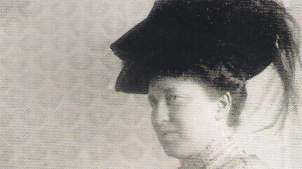 Schwarz-weiß-Abbildung von Julie Bassermann. Sie ist von der Seite zu sehen, trägt einen dunklen Hut und ein langes Kleid.