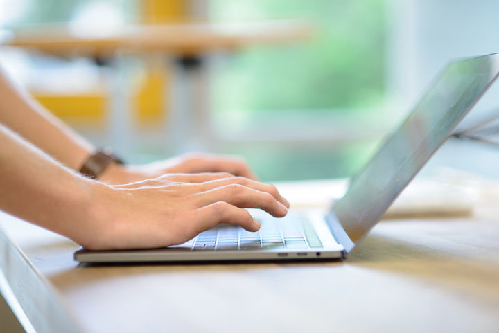 An open laptop is on the table and two hands are typing on it. 