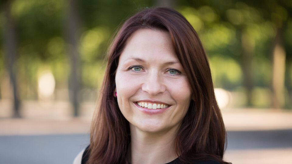 Portrait von Sabine Carey. Sie trägt eine schwarze Bluse und steht lächelnd vor einem Park.