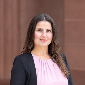 Larisa Czajka hat dunkle lockige lange Haare. Sie trägt ein rosanes Oberteil und ein dunkles Jacket.
