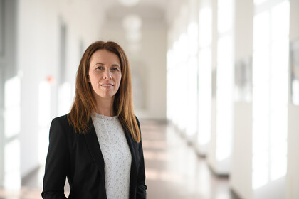 Eine Person trägt eine weiße Bluse sowie einen schwarzen Blazer und steht in einem Flur. Die Person heißt Alexandra Niessen-Ruenzi.
