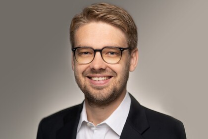 Portrait von Marc Lerchenmüller. Er trägt ein weißes Hemd sowie einen schwarzen Blazer und lächelt.