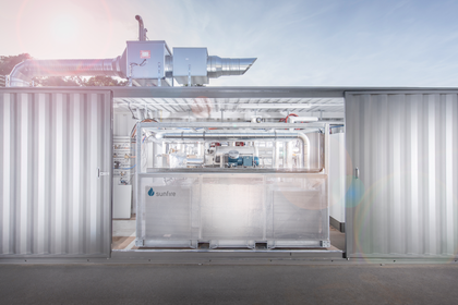 Eine industrielle Elektrolyseanlage mit der Aufschrift "Sunfire" steht zwischen zwei Containerwänden.