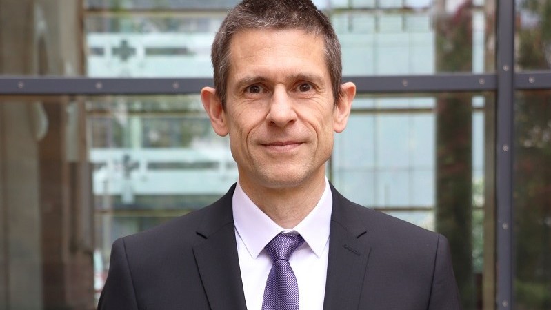 Portrait von Martin Schlather. Er trägt einen dunklen Anzug, ein weißes Hemd mit Krawatte und blickt leicht lächelnd in die Kamera.
