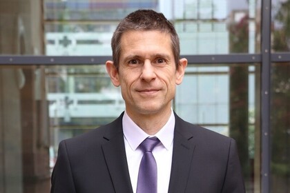 Portrait von Martin Schlather. Er trägt einen dunklen Anzug, ein weißes Hemd mit Krawatte und blickt leicht lächelnd in die Kamera.