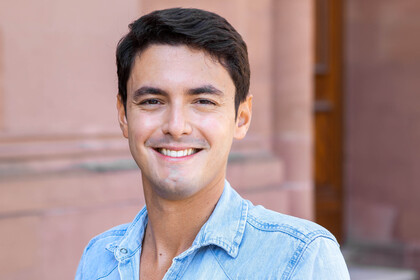 João Areal auf dem Ehrenhof des Schloss Mannheim. Er hat kurze schwarze Haare und trägt ein hellblaues Jeanshemd.