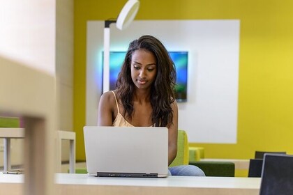 Eine Studierende hat lange braune Haare und trägt ein gelbes Oberteil. Sie sitzt vor ihrem Laptop.