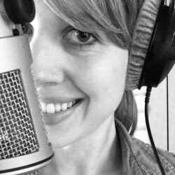 Schwarzweißfoto einer lächelnden Frau vor einem Mikrofon mit Kopfhörern auf den Ohren. 