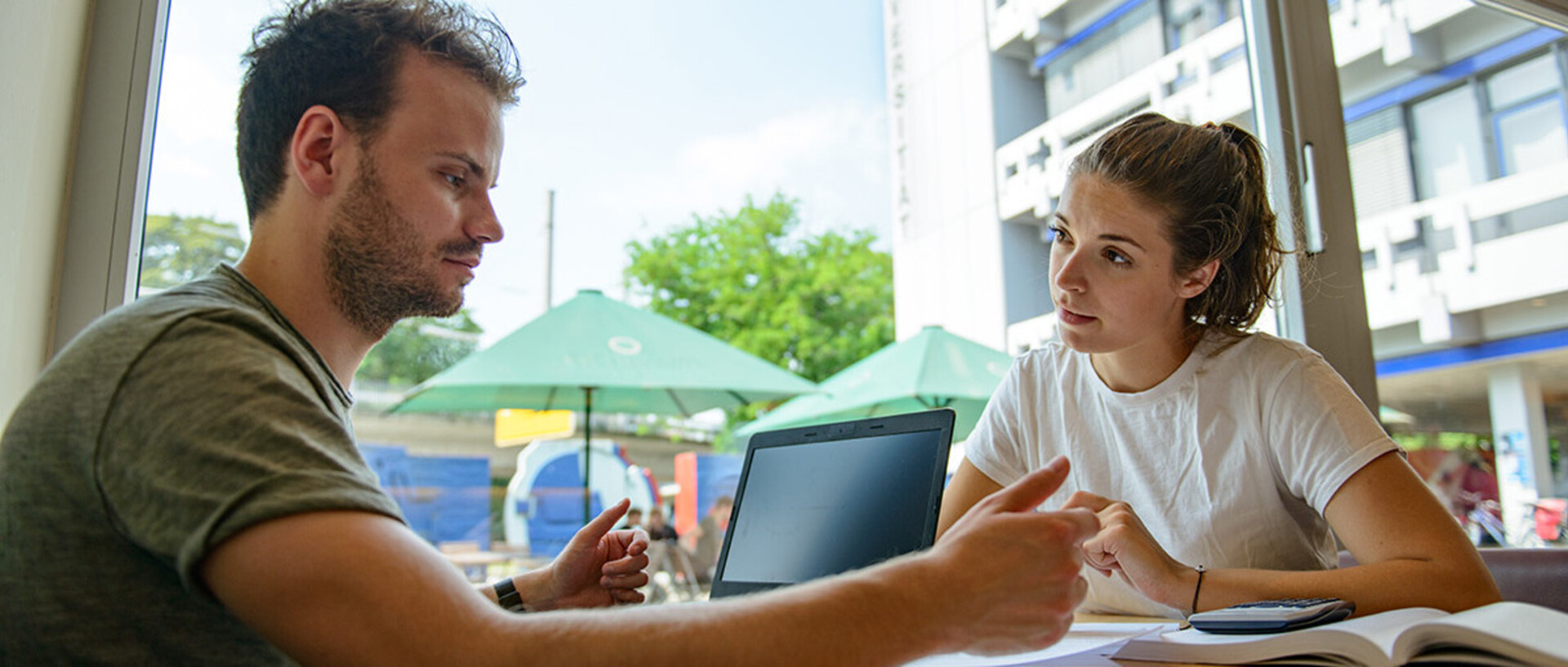 Eine Studentin und ein Student lernen gemeinsam an einem Tisch im Café Soleil.