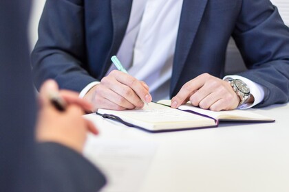 Person in Anzug schreibt in ein Notizbuch