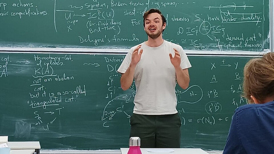 Ein junger Mann steht für einer Tafel und sprich zur Klasse