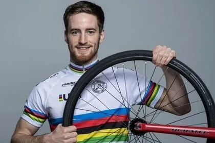 Serafin Schefold hat kurze Haare und trägt ein Sport-Trikot. Er hält ein Fahrrad-Rad in der Hand und lächelt
