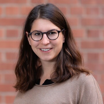 Miriam Gohl hat lange braune Haare. Sie trägt eine runde schwarze Brille und ein beiges Oberteil.
