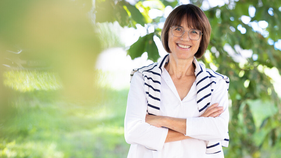 Prof. Dr. Annette Kehnel. Sie steht lächelnd unter einem Baum, dabei trägt sie eine Brille und eine weiße Bluse, ein gestreifter Pullover liegt um ihre Schultern.