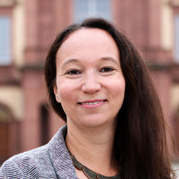 Vania Fundinger-Sawant hat braune lange Haare und trägt einen grauen Blazer.