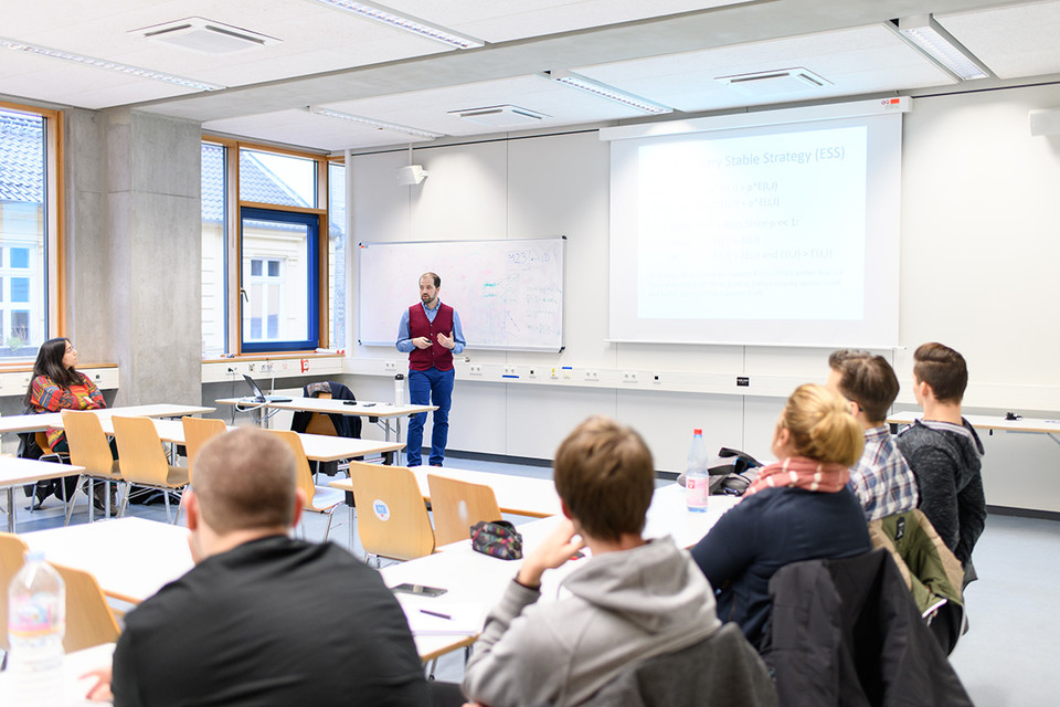 Dozent unterrichtet in einem Seminar, das Publikum hört ihm zu.