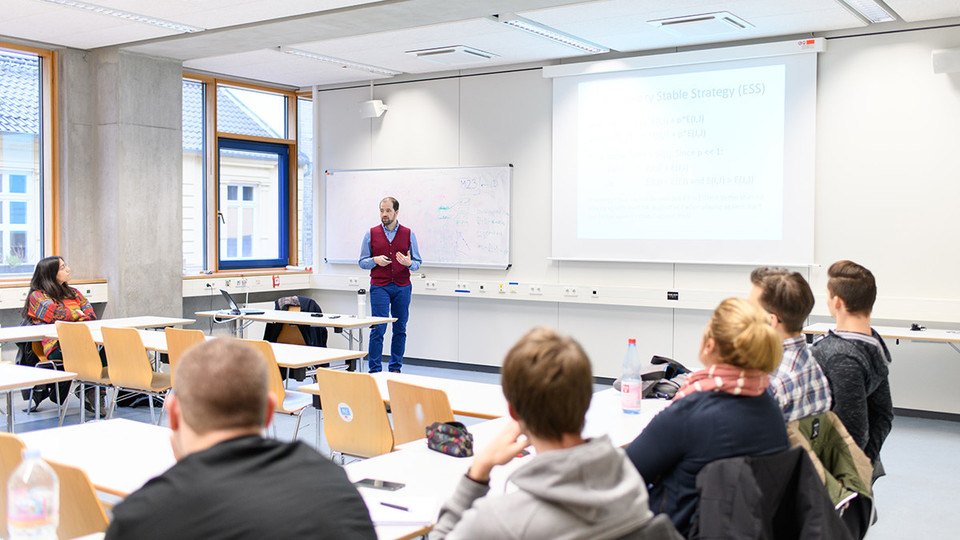 Dozent unterrichtet in einem Seminar, das Publikum hört ihm zu. 