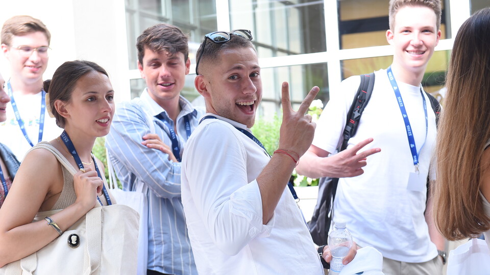 Fünf lächelnde Personen tragen schicke Kleidung und stehen nebeneinander. Alle tragen einen Lanyard der Universität LUIIS.