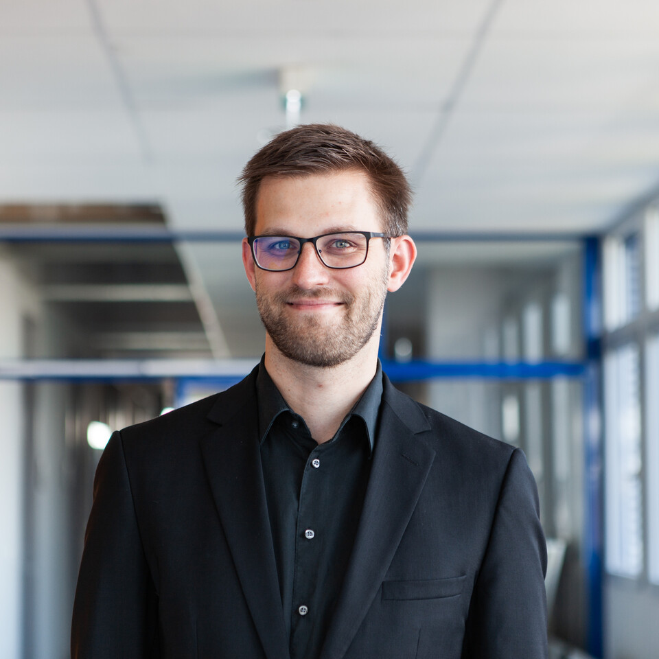 Porträt von Herrn Janke. Er trägt eine Brille und ein schwarzes Hemd.