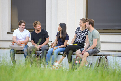 Mehrere Studierende sitzen auf einer Bank und unterhalten sich. 