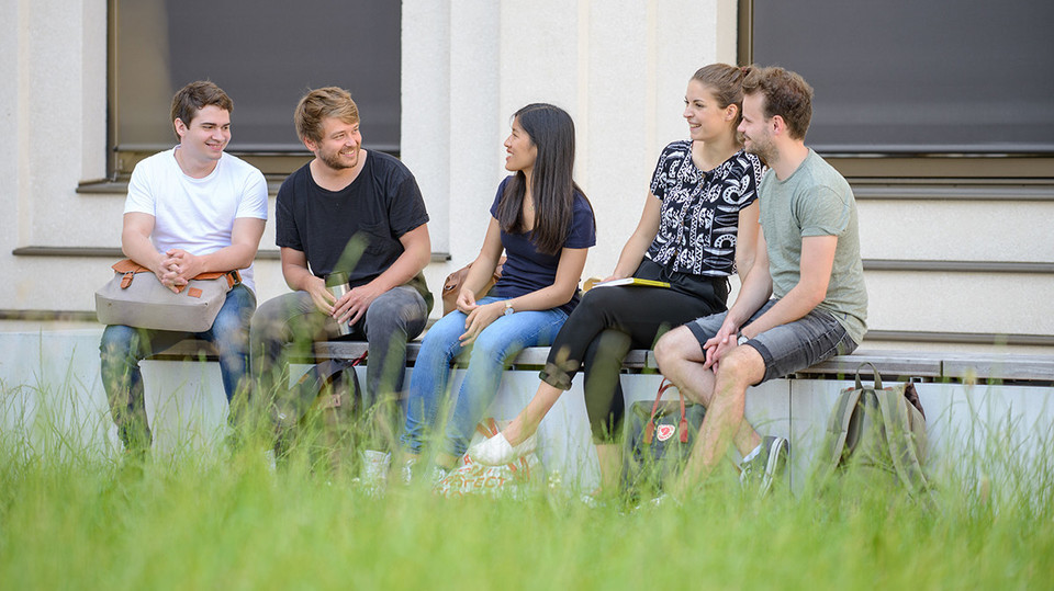 Mehrere Studierende sitzen auf einer Bank und unterhalten sich. 