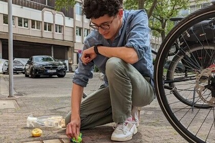 Ein junger Mann kniet auf einem Gehweg an einer Straße. Mit einem Tuch säubert er drei goldfarbene Stolpersteine, die in den Boden eingelassen sind. Link: Instagram-Post Einblicke in den Master Geschichte
