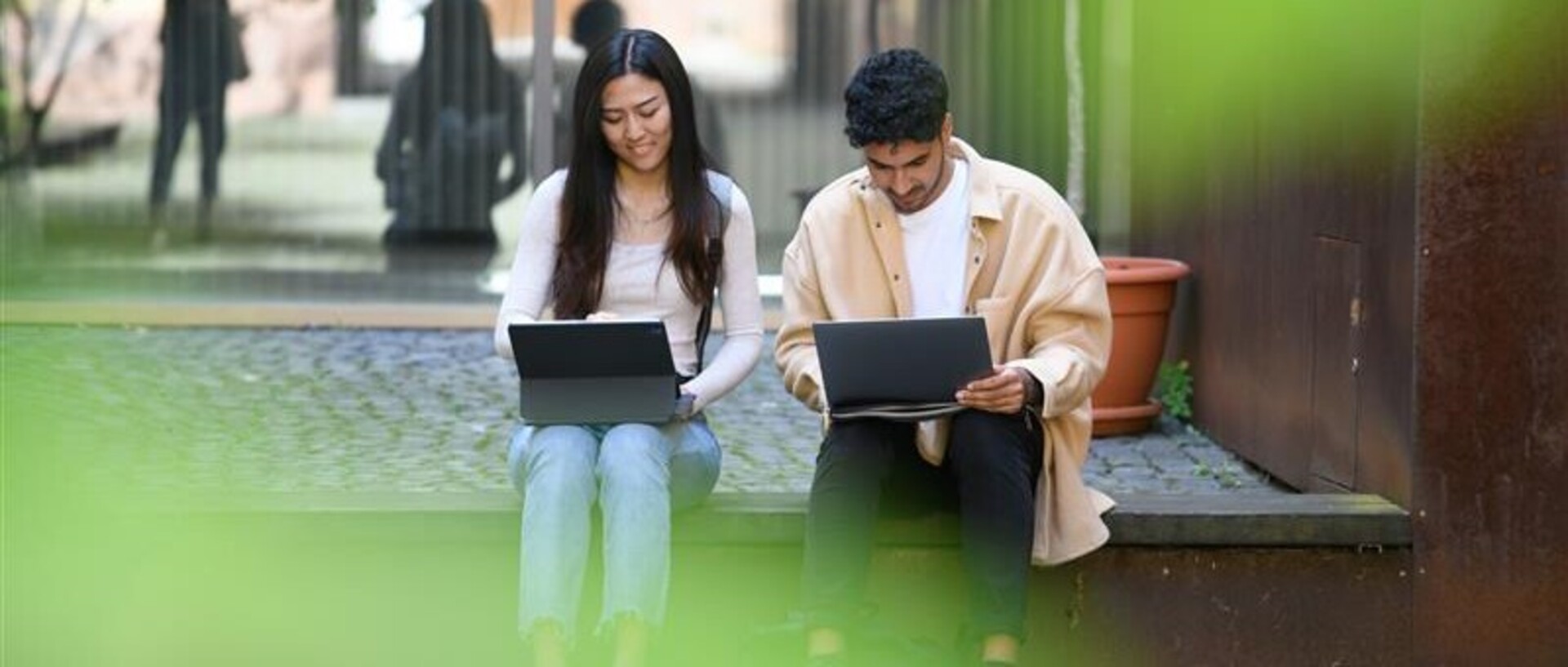 Zwei Studierende sitzen neben einander und schauen auf ihre Laptops.