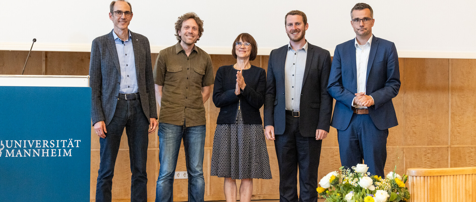 Fünft Menschen in festlicher Kleidung stehen auf einer Bühne.